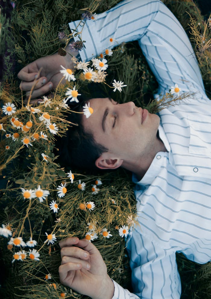 A man in a dress shirt lying in a chamomile field, eyes closed, enjoying relaxation.