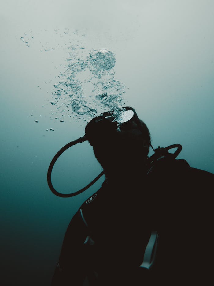 Silhouette of diver releasing bubbles underwater, capturing the essence of deep-sea exploration.