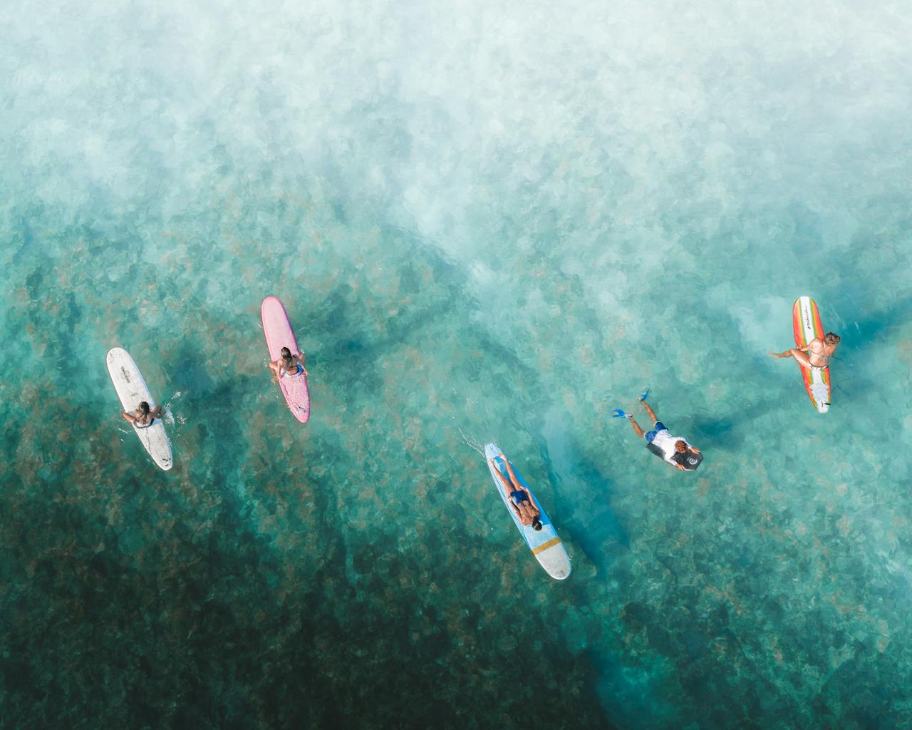 Top-down view of surfers paddling on surfboards in crystal clear ocean waters.